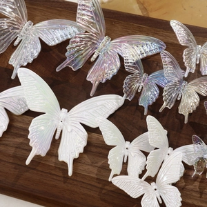 Iridescent purple and pearl white acrylic butterfly charms on a textured wooden background