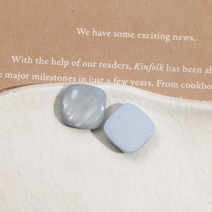 Macro detail of square resin earrings featuring mother of pearl and matte blue finish