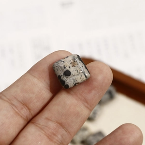 Detailopname van vierkante dalmatiër jaspis kralen voor DIY sieraden tussen de vingers