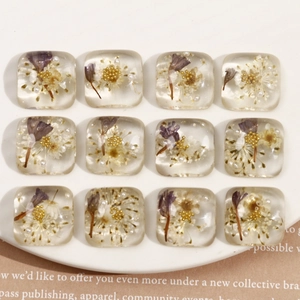Vue à plat de 12 breloques carrées en résine avec fleurs séchées et fausses perles