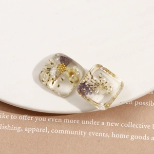 Détail macro de boucles d'oreilles carrées en résine avec fleurs séchées et perles