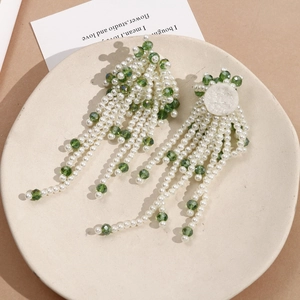 Detail of elegant long tassel earrings with white pearls and emerald green glass beads