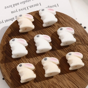 Close-up of eight cute white flocked rabbit beads for DIY jewelry on a wooden tray