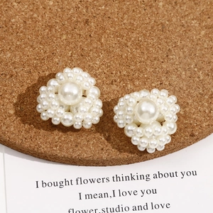 Detail shot of heart-shaped pearl cluster earrings on a dark cork stand with a quote card