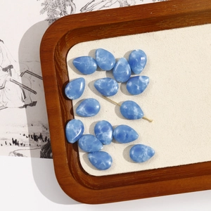 Macro shot of blue larimar water drop beads with gold pin on beige velvet tray