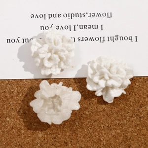 Three white handmade 3D flocked carnation flower DIY accessories on cork background