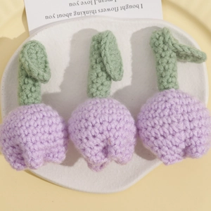 Detail of three handmade crochet light purple tulip pendants on a white ceramic plate