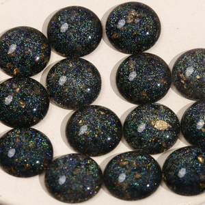 Macro shot of 13 black starry resin cabochons with sparkling glitter and gold foil accents