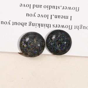 Close-up of round black resin stud earrings with starry sky glitter and sequins