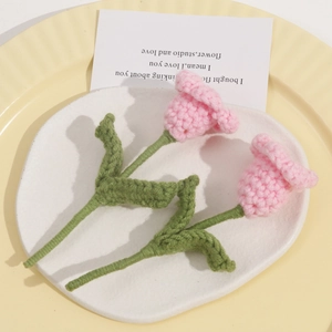 Handmade crochet pink tulip flower brooches on a ceramic plate with warm lighting
