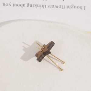 Macro shot of star-shaped brown wood earring with gold pins on a white ceramic plate