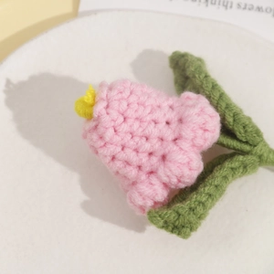 Detailed texture of a handmade pink crochet tulip flower with green leaves and yellow stamen