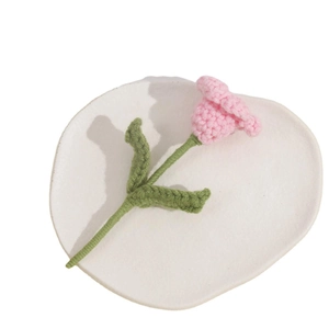 Handmade crochet pink puff flower with green leaves on a white ceramic tray