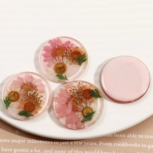 Detailed view of handmade round resin charms with real dried pink and orange daisies