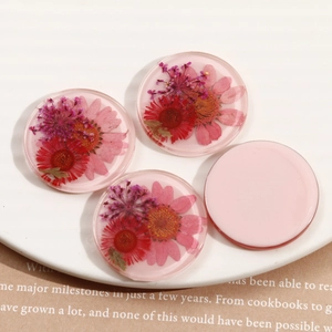 Detailed macro of round resin charms with embedded red dried flowers for DIY jewelry crafts