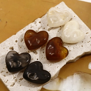 Macro shot of ink marble heart resin charms in cream, amber, and grey on white travertine