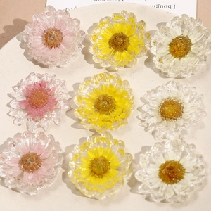 Dettaglio di ciondoli a margherita in resina con veri fiori secchi in bianco, giallo e rosa