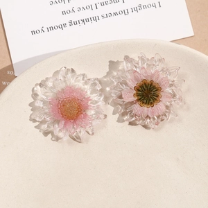 Dettaglio di due ciondoli a margherita in resina con fiori secchi rosa fatti a mano