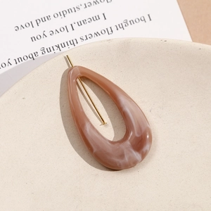 Detail of marble pattern resin earring component with golden metal pin on beige plate