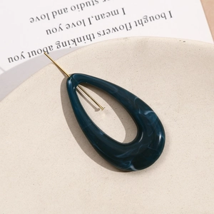 Detail of dark blue marble resin hair pin with gold metal needle on beige ceramic tray