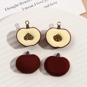 Macro shot of sliced resin apple charms with gold hooks on a ceramic plate for DIY jewelry