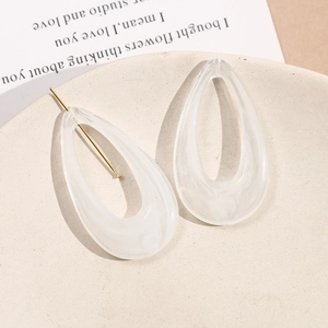 Elegant teardrop acrylic earrings with white marble texture and gold pins on stone tray