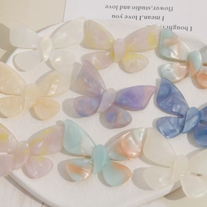 Gradient acetate butterfly hair accessories in cream and pastel colors displayed on a tray