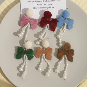 Macro detail of long flocking bow earrings with pearl tassels in six vibrant colors