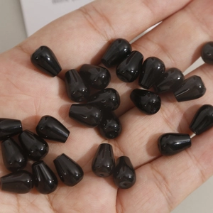 Detailed view of polished black teardrop beads with top-drilled holes for DIY jewelry