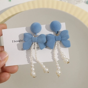 Detail of blue flocked bow earrings featuring elegant dangling white pearl tassels
