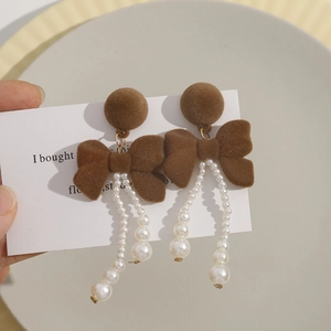 Detailed close-up of brown flocked bow earrings with elegant white pearl tassels