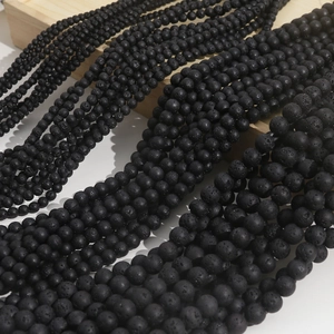Natural black lava stone beads for jewelry making in various sizes on a wooden surface