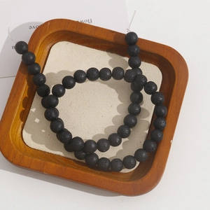 Macro shot of 8mm matte black lava stone beads with porous texture in a wooden tray
