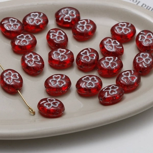 Macro view of red oval glass beads with silver clover patterns for DIY jewelry