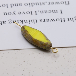 Macro detail of oval Czech glass bead with yellow patterns and gold metal loop for DIY jewelry