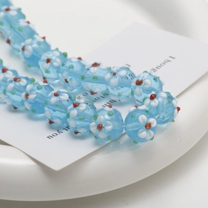 Close-up of light blue glass beads with delicate floral patterns for DIY jewelry making