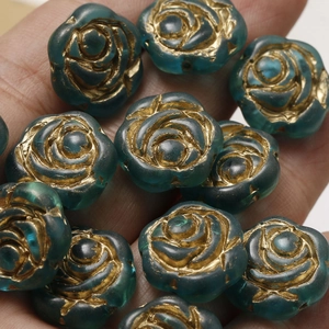 Detailed macro view of vintage blue-green rose beads with gold edges held in a palm