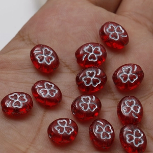 Macro shot of red glass oval beads with silver clover patterns for DIY jewelry making