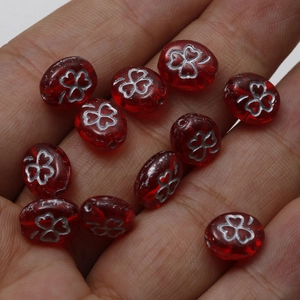 Macro shot of vintage red oval Czech glass beads with silver clover motif on hand