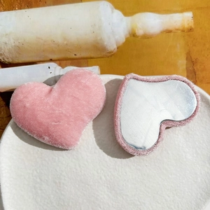 Pink velvet heart-shaped portable makeup mirror with soft plush texture in white ceramic tray
