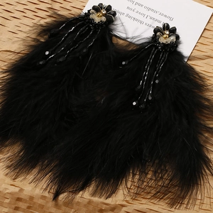 Elegant black feather earrings with crystal flower and golden bow on textured background