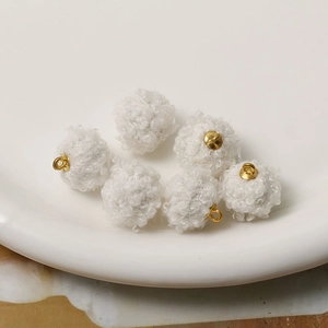Close-up of white faux lamb wool ball charms with golden metal loops for DIY jewelry making