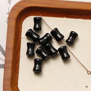 Macro detail of black waist-drum beads on a metal needle for DIY jewelry making