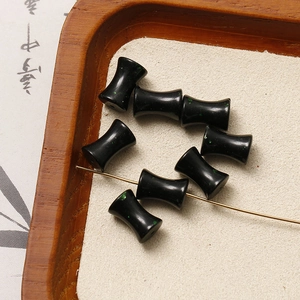 Macro detail of black drum-shaped beads with green speckled texture for DIY jewelry making