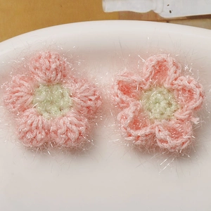 Nahaufnahme von handgehäkelten rosa Puffblumen mit glitzerndem Silberfaden und grünem Kern