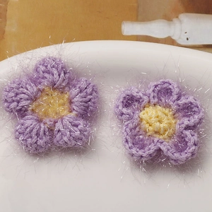 Nahaufnahme von häkelblumen in lila und gelb mit glitzerndem silberfaden und flauschiger optik