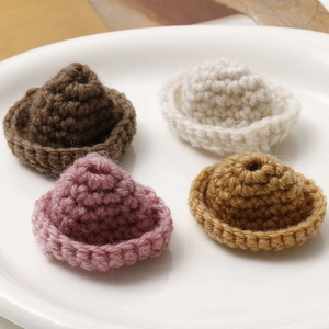 Detailed macro view of four mini crochet hats in brown, white, pink and yellow yarn