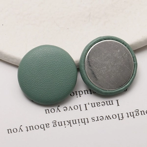 Detail view of round Morandi green litchi grain leather buttons with metal backing