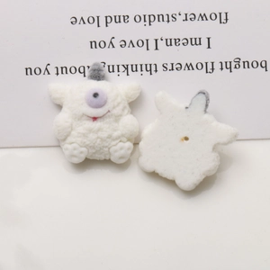 Detailed macro view of cream-colored flocked monster charms showing front and back DIY base