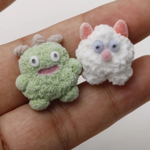 Macro shot of mini flocked monster and cat charms shown on a fingertip for scale